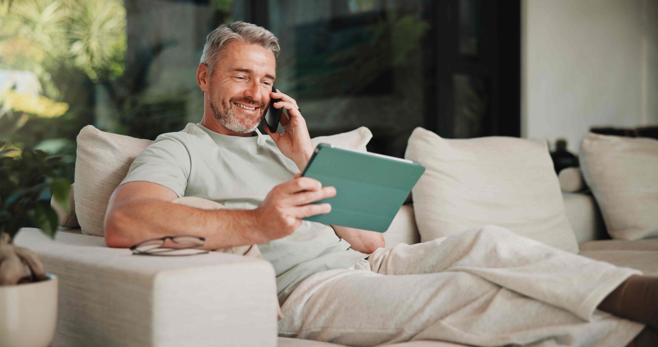 Phone call, smile and tablet for remote work with man on sofa in home living room